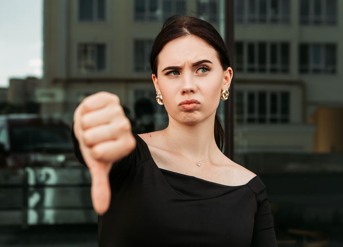 Young woman in black dress showing thumbs down gesture expressing dislike of things women do to seem attractive to men