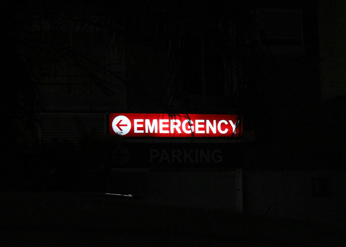 Emergency sign glowing at night outside hospital, symbolizing urgency related to patient&rsquo;s haunting final post before fatal dental procedure
