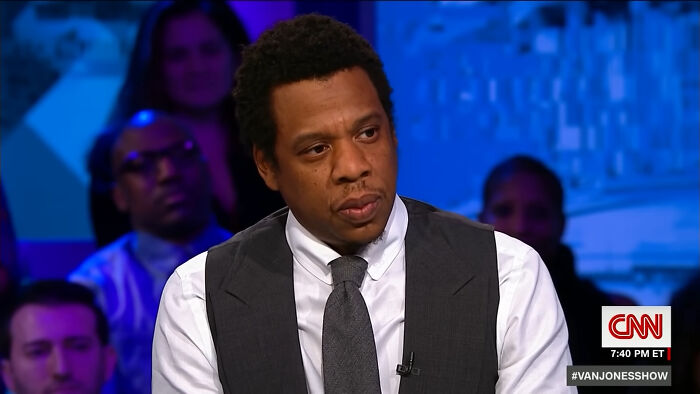 Man in a suit and tie speaking on a TV show with an audience in the background discussing celebrities and closet skeletons.