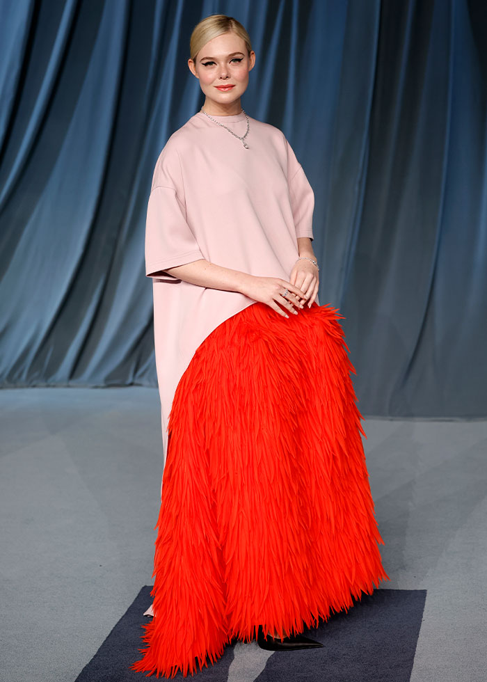 Female celebrity posing in a pink top and bright red feathered skirt showcasing 2025 celebrity fashion disasters. Female celebrity posing in a pink top and bright red feathered skirt showcasing 2025 celebrity fashion disasters.