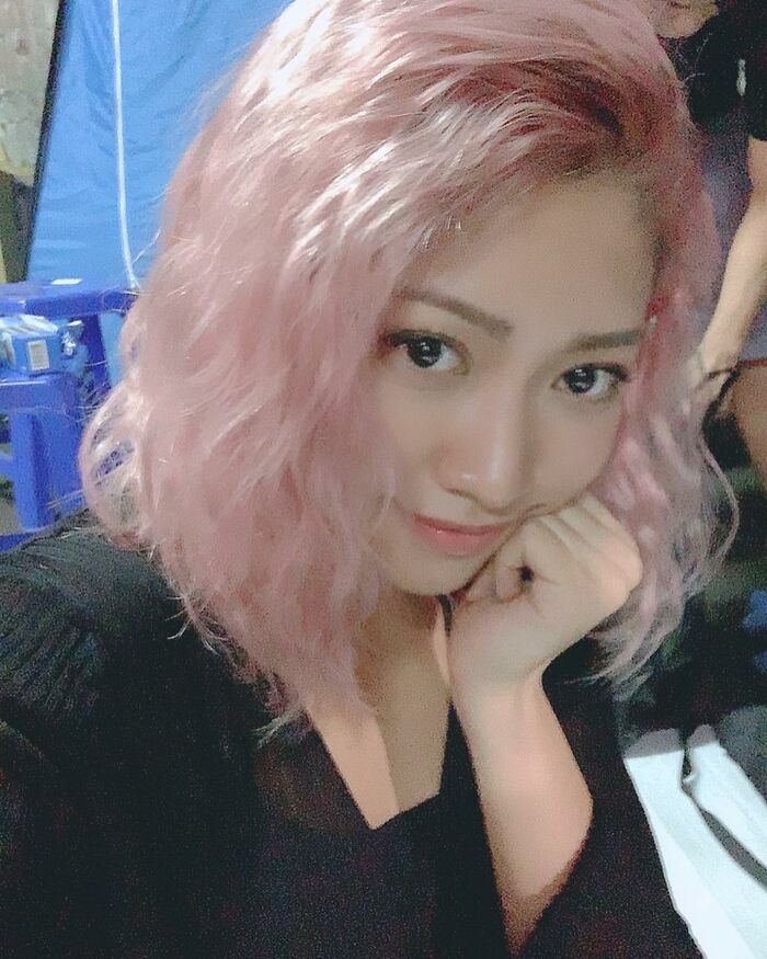 Young woman with pink wavy hair smiling in a selfie, hand on chin, representing Cancel Culture Victims