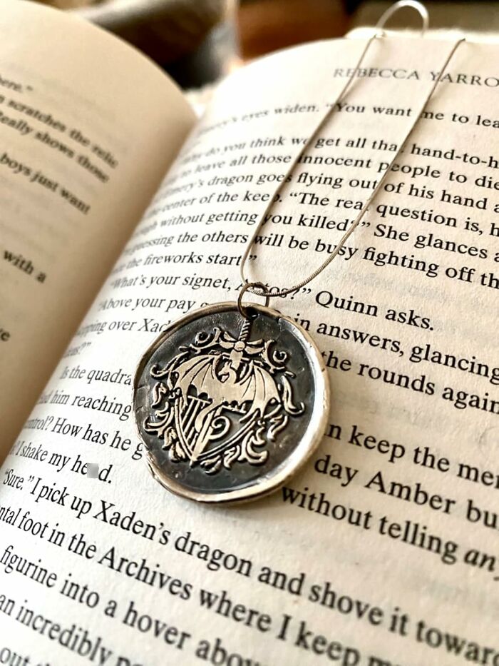 Silver pendant necklace with dragon design placed on an open book, perfect gift for personality found in an isle at Hobby Lobby.