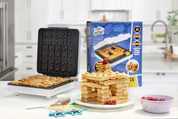 Waffle maker and unique waffle gift displayed with stacked waffles and fresh raspberries on a kitchen counter.