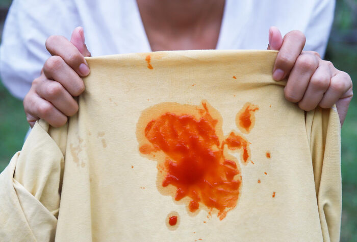 Person holding a shirt with a large ketchup stain, symbolizing revenge stories with a bitter aftertaste.