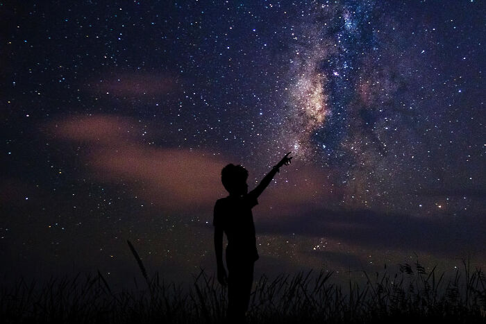 Silhouette of a person pointing at the starry night sky, illustrating disturbing science facts about the universe.