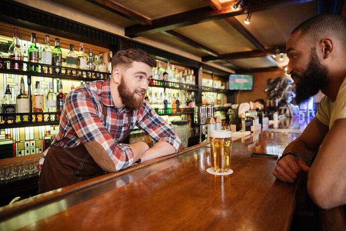 Bartender in plaid shirt chatting with customer over a pint of beer in a cozy bar, once famous regular job setting.