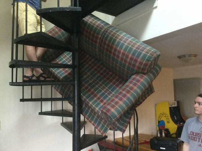 Plaid couch stuck on a spiral staircase with a person observing, a random pic that makes you laugh before you know why.