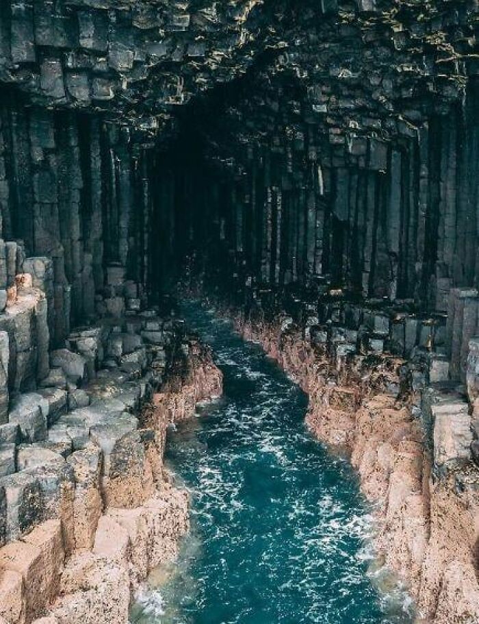 Ocean water flowing through a natural basalt rock cave with hexagonal columns, a place that looks AI generated but is real.