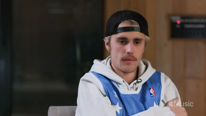 Young man in a backward cap and sports jersey sharing fascinating secrets about celebrities in an intimate interview setting.