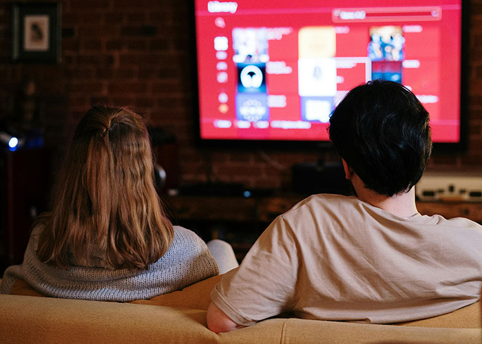 Couple sitting on couch watching TV, representing people sharing the most insane thing their ex ever did stories.