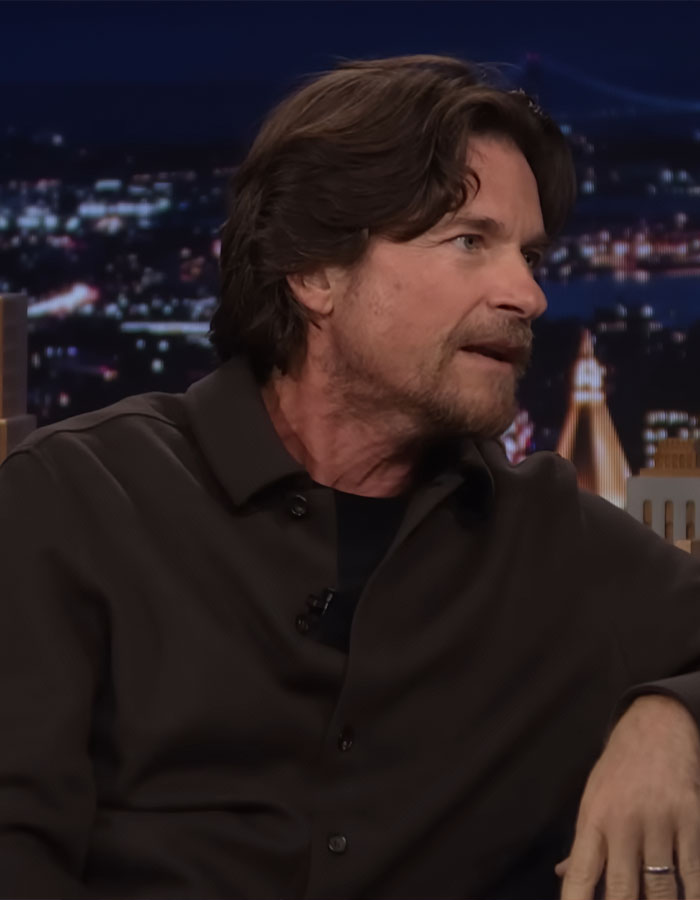 Jason Bateman in a dark shirt sharing a story during a nighttime talk show with city lights blurred in the background Jason Bateman in a dark shirt sharing a story during a nighttime talk show with city lights blurred in the background