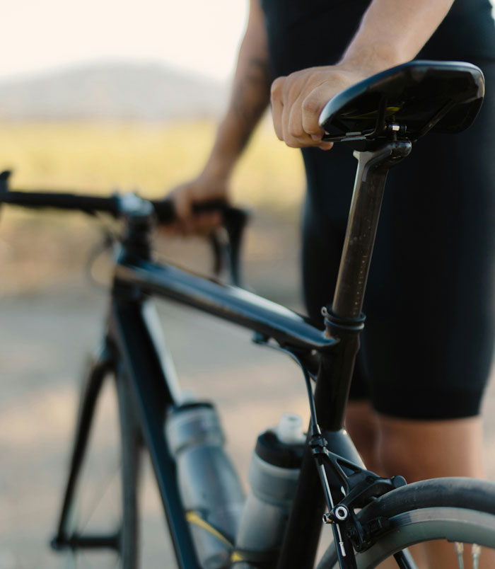 Cyclist holding a black road bike saddle and handlebar, showing details of the bike frame and gear in outdoor setting.