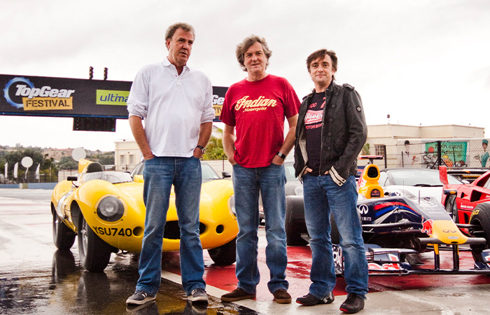 Three men standing in front of classic and racing cars at a Top Gear Festival, featured in longest running TV shows.
