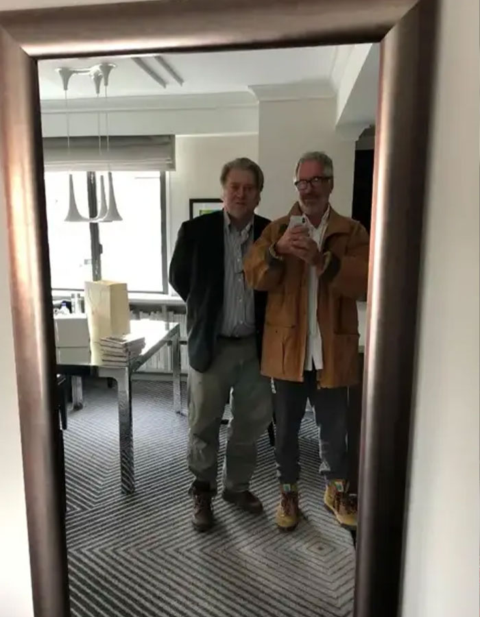 Two men standing in front of a mirror with a table and books, linked to disturbing Epstein desk photo backlash. Two men standing in front of a mirror with a table and books, linked to disturbing Epstein desk photo backlash.