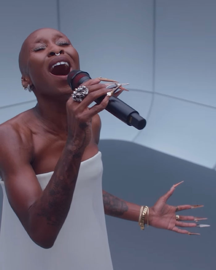 Cynthia Erivo singing passionately wearing a white dress, highlighting her oddly large hands and long nails in a performance. Cynthia Erivo singing passionately wearing a white dress, highlighting her oddly large hands and long nails in a performance.