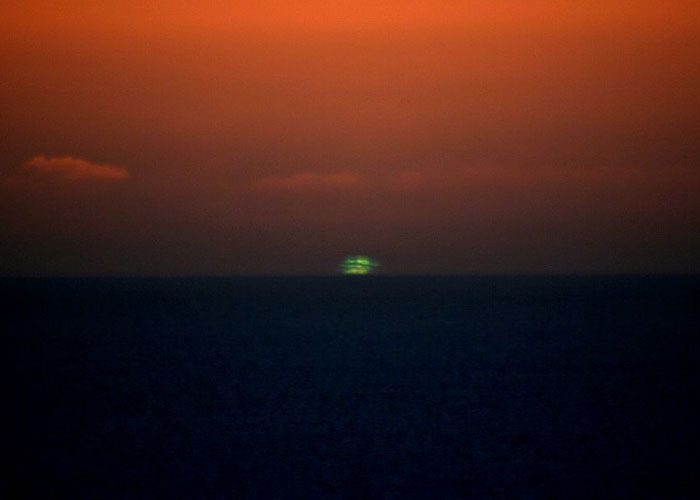 Mysterious green flash over dark ocean at sunset in a remote and isolated place with an eerie orange sky.