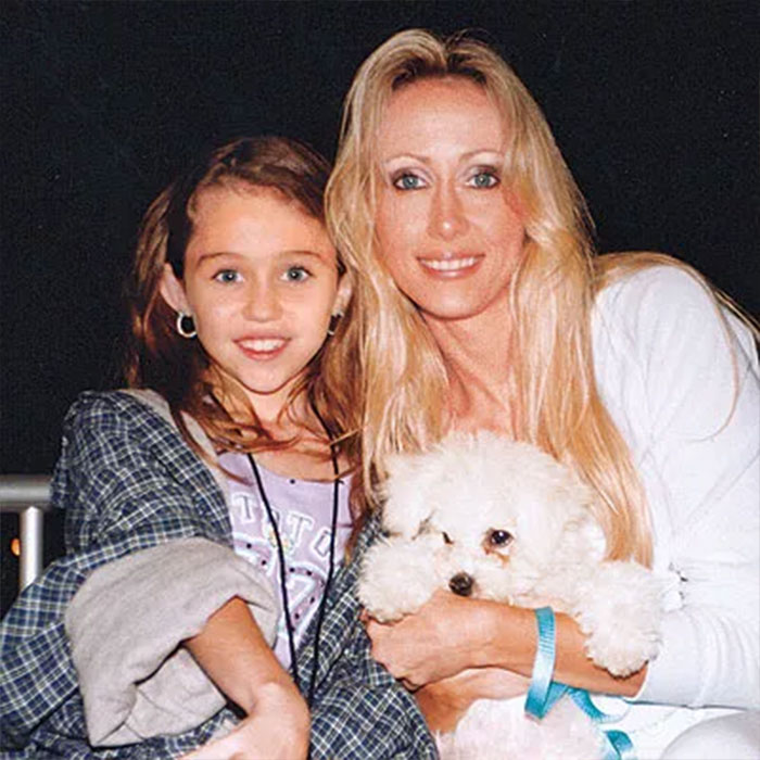 Woman claiming to be Miley Cyrus’ true birth mother with a young girl and a small white dog in a casual setting Woman claiming to be Miley Cyrus’ true birth mother with a young girl and a small white dog in a casual setting