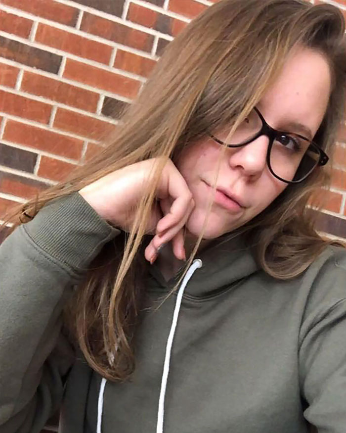 Young woman wearing glasses and a hoodie, sitting in front of a brick wall, representing engaged teacher facing consequences.
