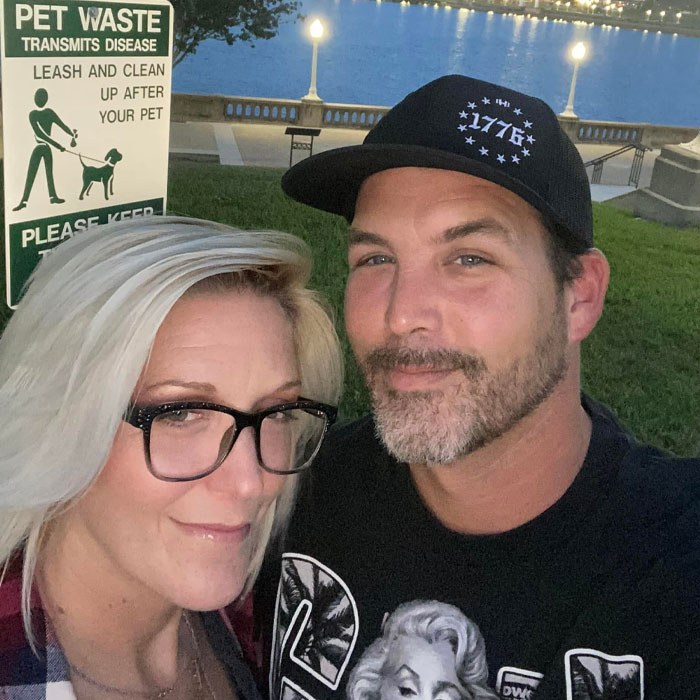 Man and woman posing outdoors near waterfront at dusk with pet waste sign in background during family gathering. Man and woman posing outdoors near waterfront at dusk with pet waste sign in background during family gathering.