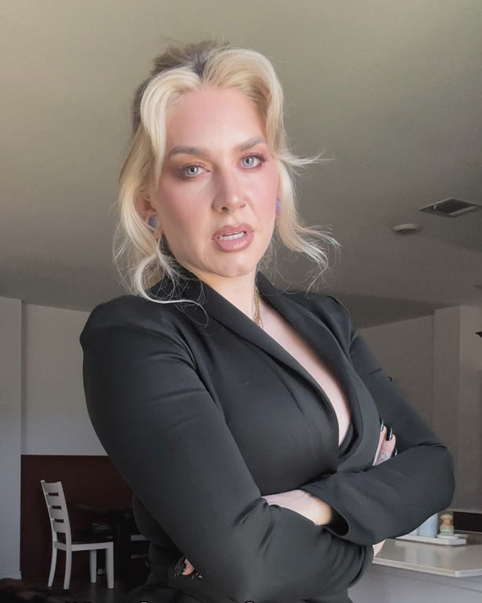 Woman with crossed arms and intense expression indoors, related to internet divided over man punishing her on flight seat switch.