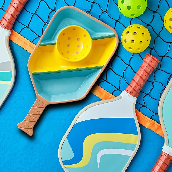 Colorful pickleball paddles and balls arranged on a net, showcasing unique never-before-seen gifts.