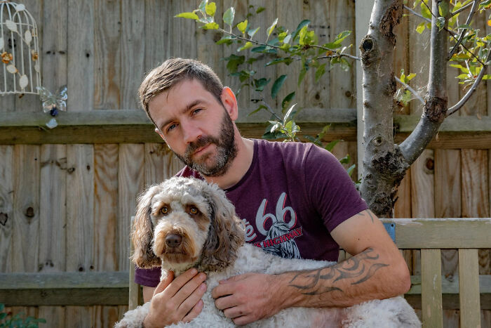 Man with beard sitting outside on a bench holding a dog, reflecting on men missed delivery babies experiences.