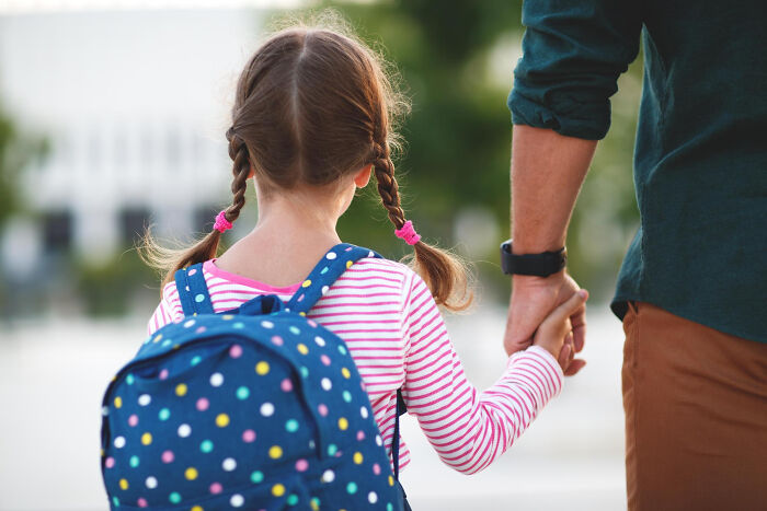 Man holding hands with a young girl wearing a polka dot backpack, representing men missed delivery babies moments.
