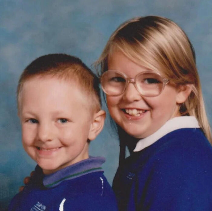 Two kids in matching blue school uniforms smiling awkwardly for a hilariously awkward childhood photo.