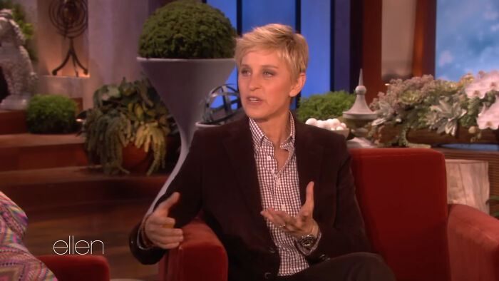 A talk show host seated on a red couch sharing fascinating secrets about celebrities during an interview segment.