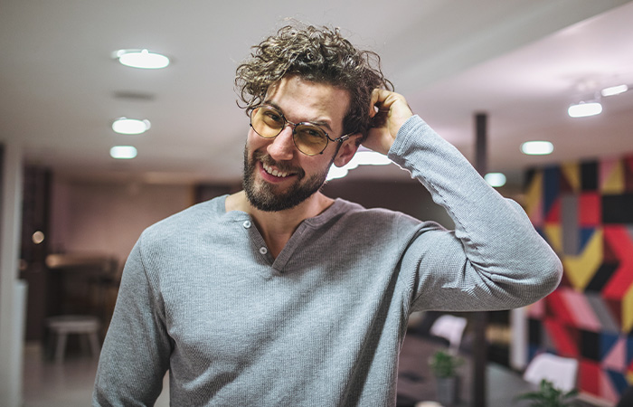 Man with curly hair and glasses smiling indoors, representing what men find attractive in women traits concept.