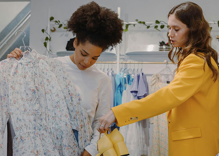 Two women examining luxury clothing and shoes in a boutique, illustrating luxury industries and expensive fashion rip-offs.