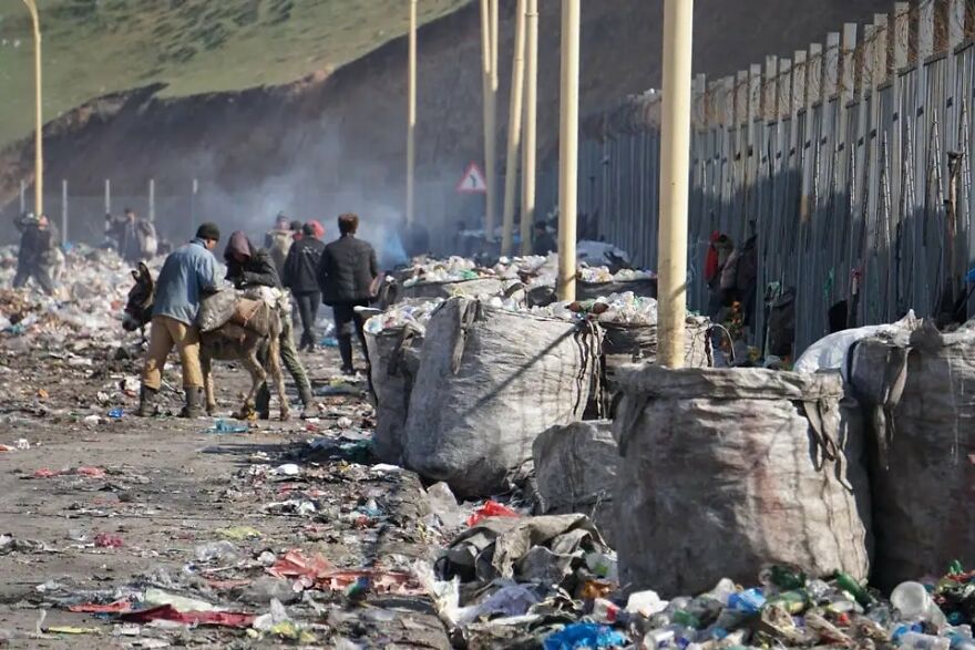 People walking through trash and large bags of waste along a polluted street in one of the dirtiest countries by pollution rankings.