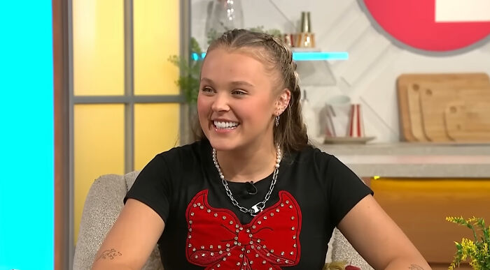 Young smiling celebrity in a casual black shirt with red bow design, discussing challenges celebrities people think suffer.