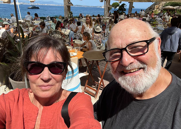 Man and woman wearing sunglasses smiling at outdoor seaside caf&eacute; with Nick Reiner received startling diagnosis concept.
