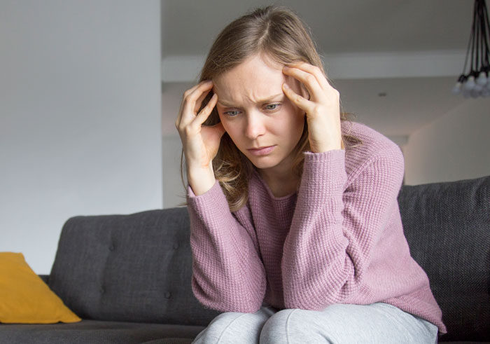 Young woman looking distressed on a couch, reflecting over man shaming her love for fiction and lowering her IQ.