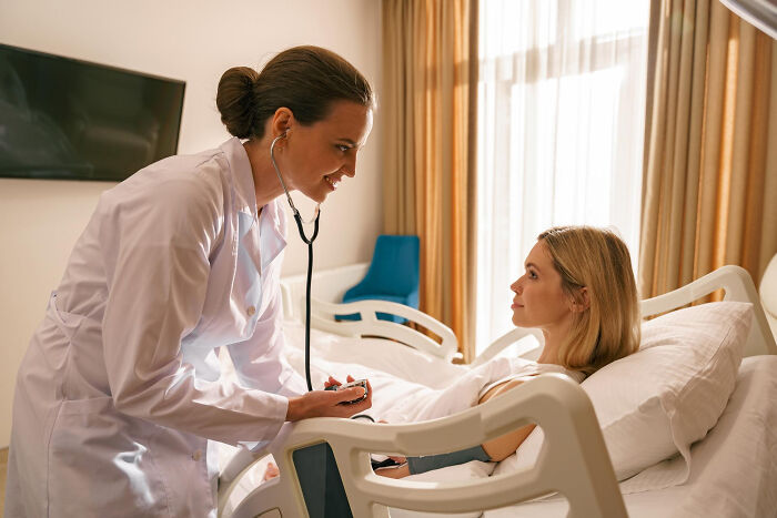 Female doctor using stethoscope to check woman in hospital bed, highlighting men missed delivery babies concerns.