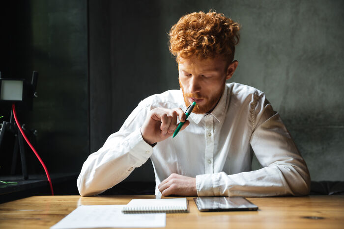 Young man in white shirt thoughtfully writing and reflecting on crazy things people have done to make their ex pine for them.