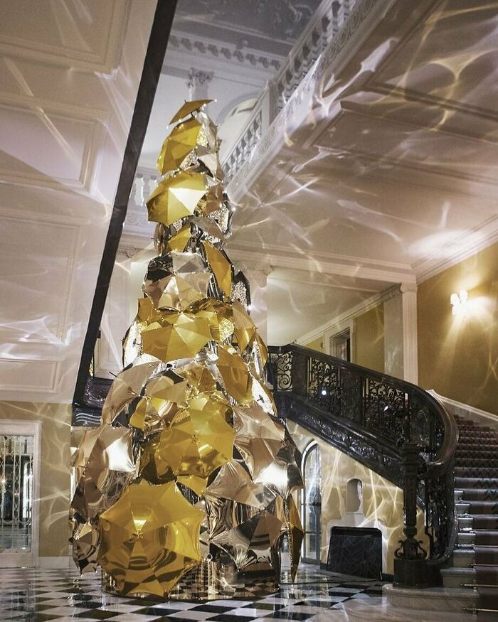Creative Christmas decorations in a workplace featuring a golden reflective tree under an ornate staircase with dramatic lighting effects.