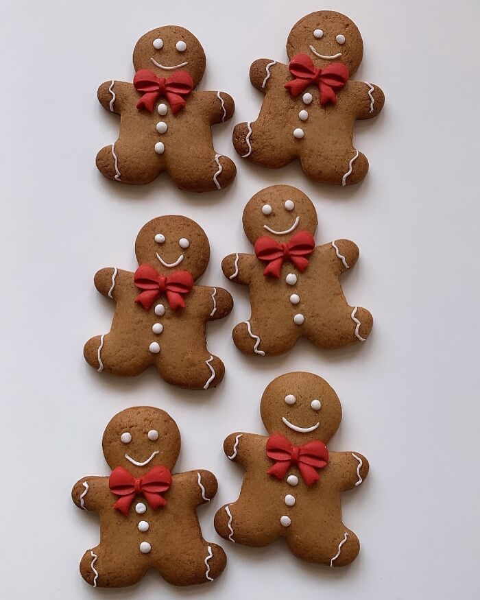 Six gingerbread cookies decorated with white icing and red bows, a popular Christmas dessert from around the world.