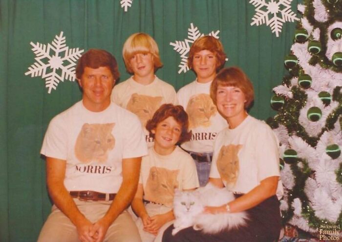 Family in matching cat shirts posing for an awkward family Christmas photo with a white Christmas tree and large snowflake decorations.