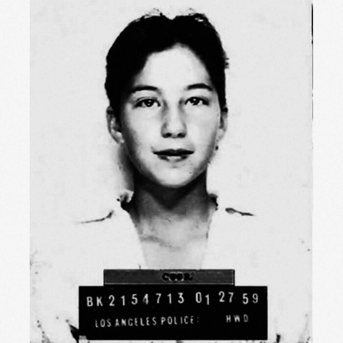 Young woman in a vintage celebrity mugshot holding a board with arrest details from Los Angeles Police Department.