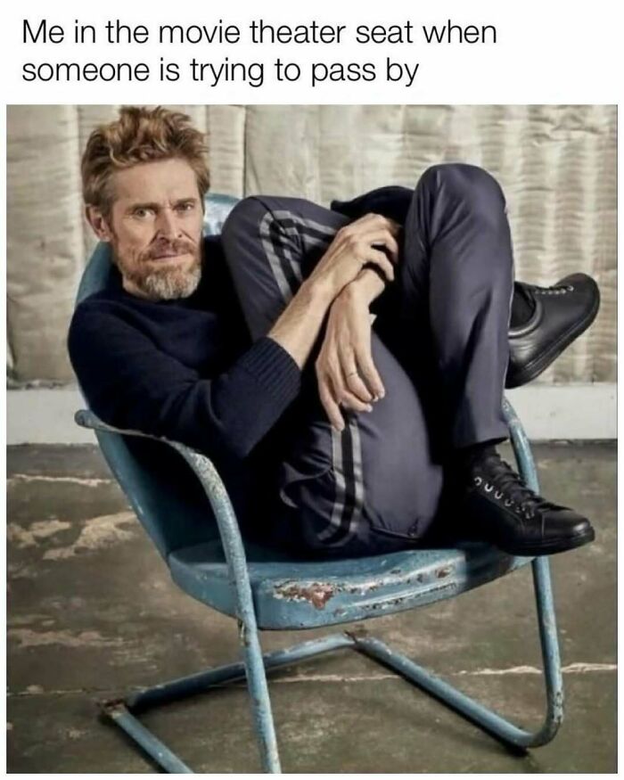 Man curled up awkwardly in a worn chair, captioned about movie theater seat, highlighting random memes to spice life up.