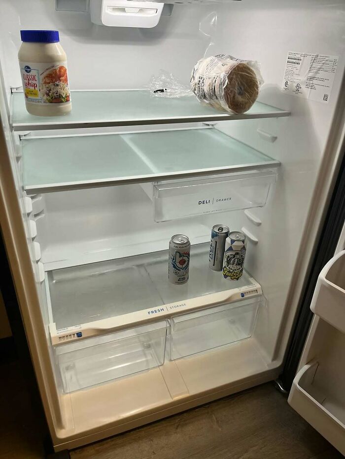 Partially stocked dude fridge with a few drinks, mayonnaise, and bread inside a mostly empty refrigerator.
