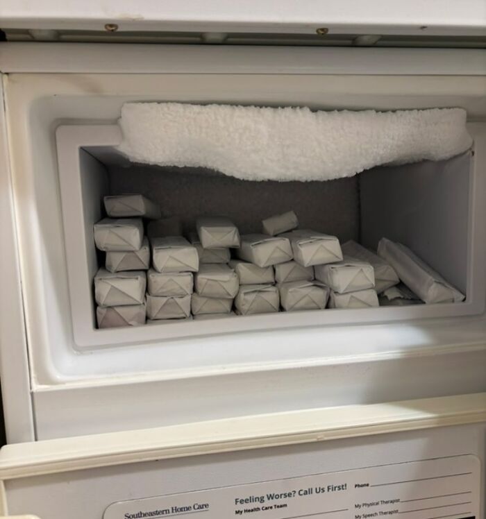 Freezer compartment of a dude fridge packed with multiple neatly stacked rectangular wrapped items and frost buildup inside.