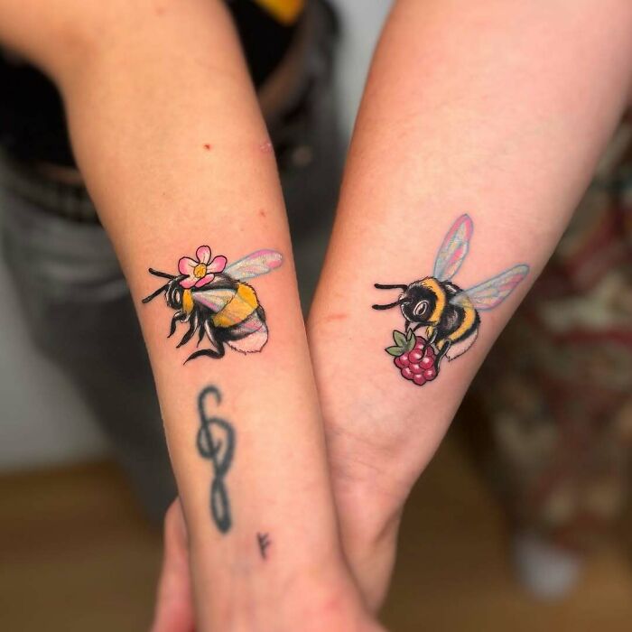 Matching wholesome tattoos of bees with a flower and a berry on two forearms showing meaningful ink.