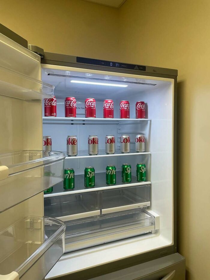 Open dude fridge neatly organized with Coca-Cola, Diet Coke, and Sprite cans on clean white shelves.