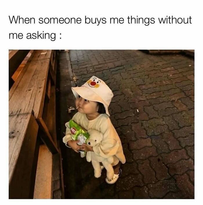 Toddler holding snacks and a teddy bear with a happy expression, illustrating humor in reality memes.