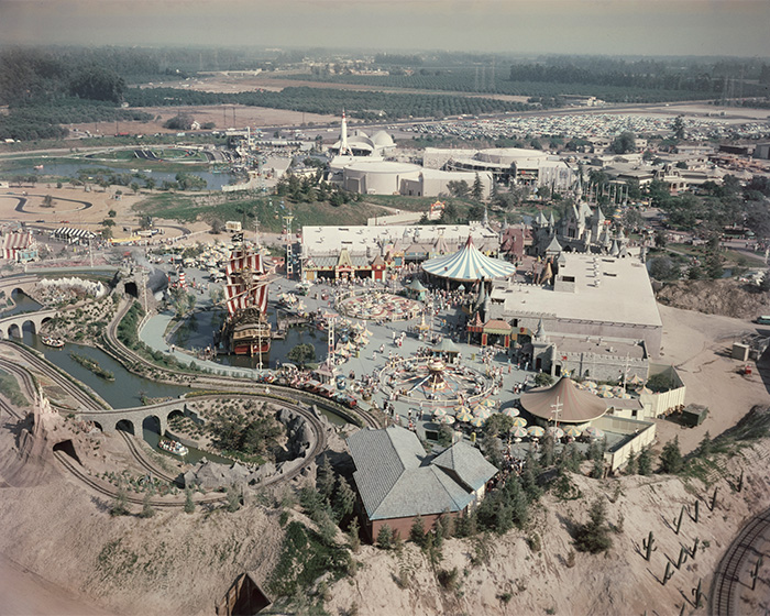 A rare vintage pop culture shot of an amusement park with themed rides and a large crowd in an expansive area.
