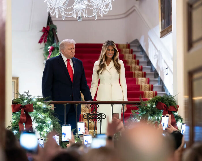 Donald Trump and Melania in a decorated hall during Christmas event, sparking outrage over bad Santa comments.