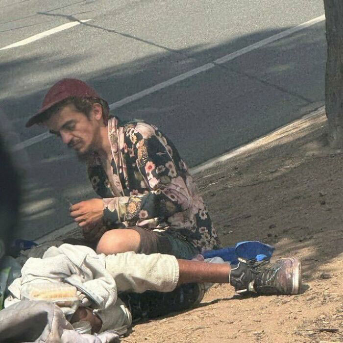Man wearing a floral shirt and red cap sitting on sidewalk near homeless person, highlighting Tylor Chase homelessness concern. Man wearing a floral shirt and red cap sitting on sidewalk near homeless person, highlighting Tylor Chase homelessness concern.